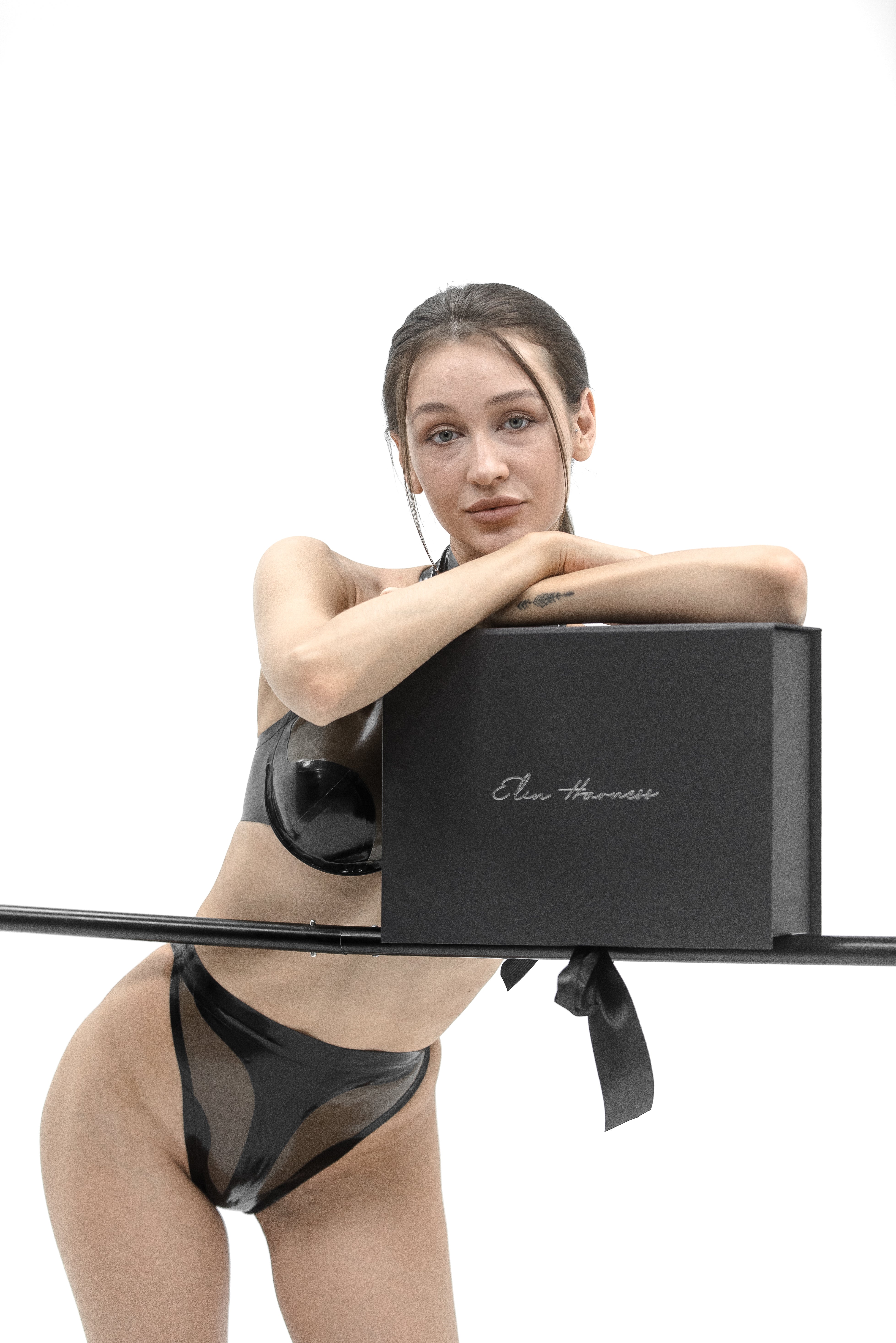Woman in black latex bikini with a black box on a white background