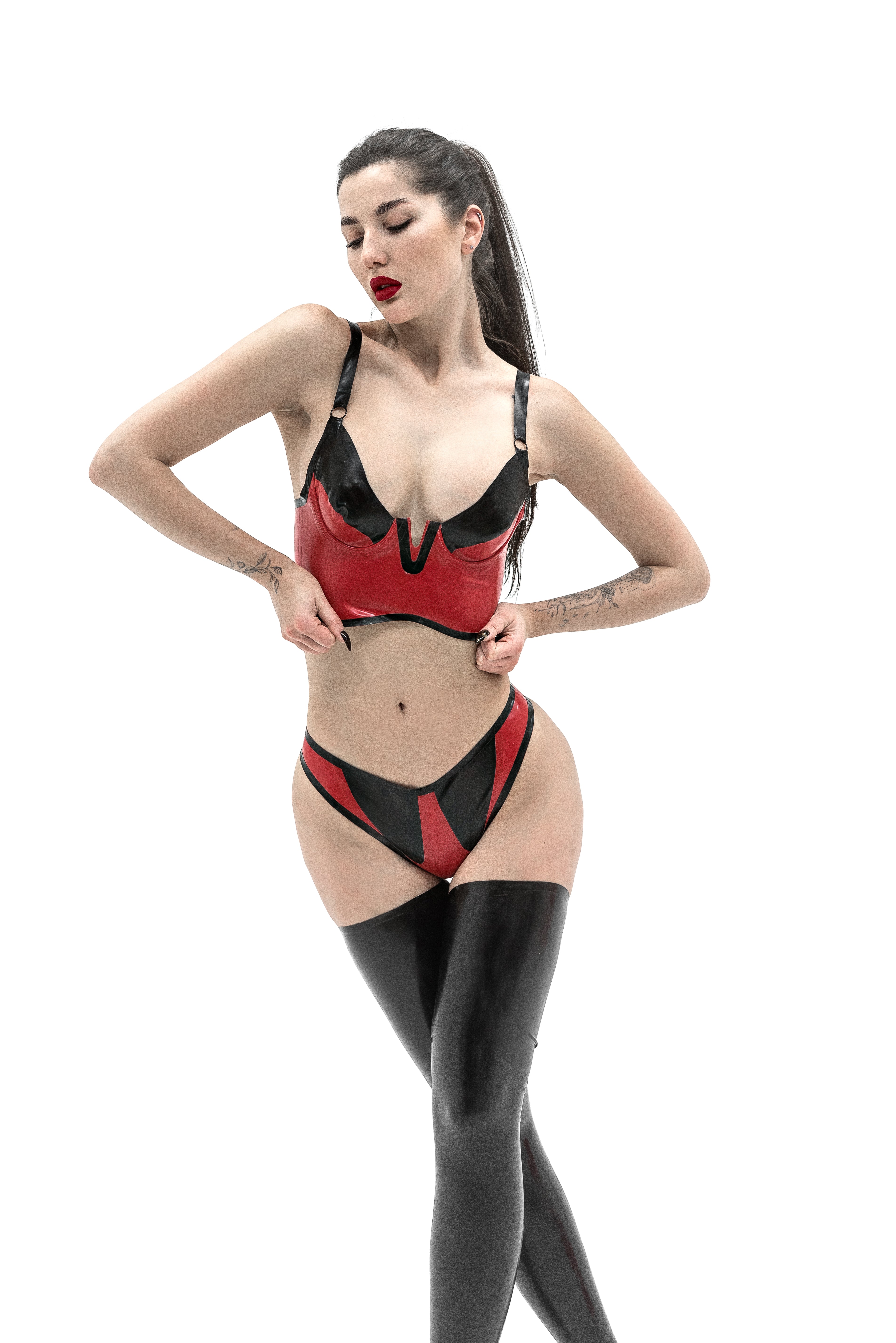 Woman wearing a red and black latex lingerie set with black stockings on a white background